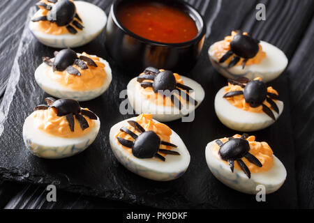 Halves deviled eggs decorated with olive spiders close-up served with ketchup on a black table. Halloween food. horizontal Stock Photo