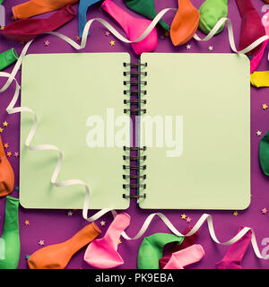 Uncovered notebook for records on a purple festive background colored balloons streamers. Top view festive background copy space Stock Photo