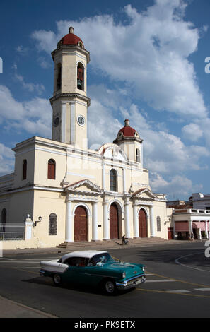 A classic vintage American 1950’s car drives past a church in Cienfuegos main square  Cuba Stock Photo