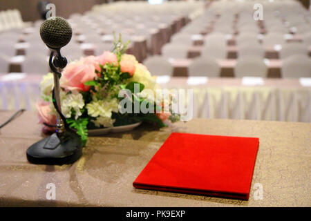 The microphone is located on podium stand at the center of the room is covered with a red carpet with a white tables cloth and chairs and prepare befo Stock Photo
