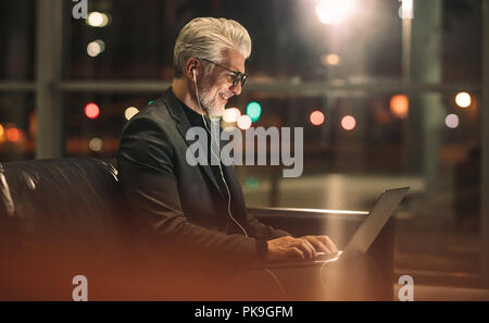 Happy mature man working late at office. Businessman using laptop in office lobby. Stock Photo
