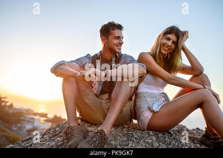 Man and woman hikers relaxing on hill top. Hiker couple taking a break sitting on rock and smiling. Stock Photo