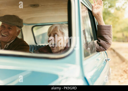 Senior woman enjoying road trip with her husband. Excited old female raising her hand out of the car and laughing. Senior couple enjoying on their roa Stock Photo