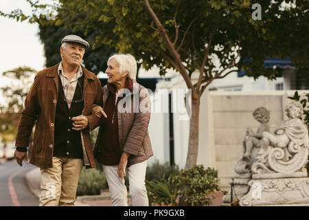 Portrait of happy retired man and woman wearing warm clothing walking together outdoors on city street. Senior couple enjoy a walk together on a winte Stock Photo