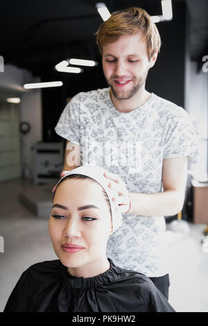 Hairdresser wrapping towel on customer's head. Brunette woman getting hair treatment in a salon. Stock Photo