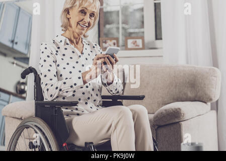 Blue-eyed woman holding her phone sitting in wheelchair Stock Photo