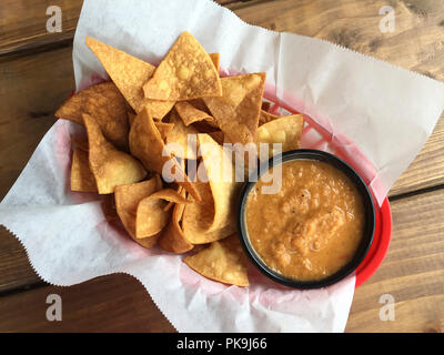 Overhead flat lay view of traditional casual Mexican snack foods tortilla chips and salsa in plastic basket lined with paper on rustic wooden table Stock Photo