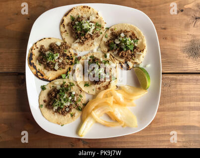Traditional Mexican foods grilled beef fajitas tacos on white ceramic plate with corn tortillas, onions, cilantro and lime garnish on wood table Stock Photo