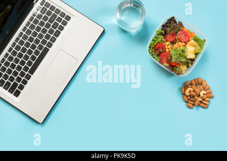 Healthy business lunch in office, salad, almonds, water on blue. Top view with copy space. Concept healthy nutrition. Lunchbox. Stock Photo