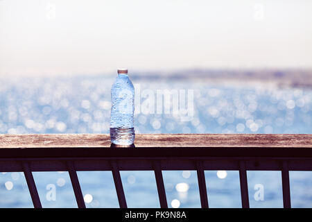Empty plastic bottle left on a pier balustrade at sunset, selective focus, color toning applied. Stock Photo