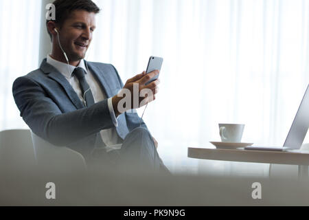 Businessman with smartphone having video call at office. Caucasian man in suit sitting at office lobby using mobile phone for making video call. Stock Photo