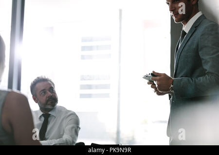 Male executive talking with colleagues during a meeting. Office workers discussing new business strategy together in conference room. Stock Photo