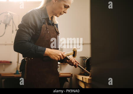 Professional female jeweler making jewelry using traditional tools in her workshop. Woman goldsmith making a ring at a workbench. Stock Photo