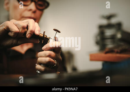 Hands of female jeweler preparing the tools for making jewelry. Senior woman hands tightening a polishing tool on grinding machine. Stock Photo
