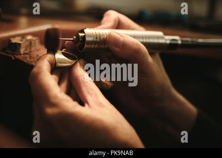 Hands of woman jeweler polishing a ring surface with grinding machine. Goldsmith making a piece of jewelry at her workbench. Stock Photo
