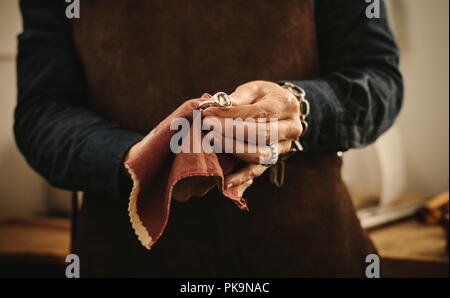 Hands of female jeweler polishing silver old-fashioned jewelry with a cloth. Jewelry maker wiping a ring with cloth at her workshop. Stock Photo