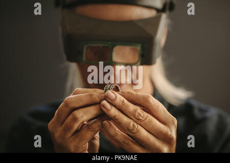 Woman goldsmith examining sliver designer ring using magnifying glass. Professional jeweler inspecting a ring using magnifying glass. Stock Photo