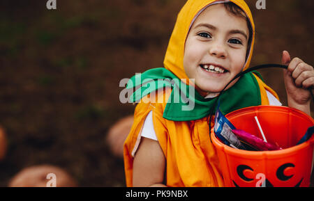 Close up portrait of cute little girl in Halloween costume holding pumpkin bucket outdoors at the park. Little girl child out for trick or treating on Stock Photo