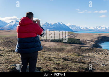Man in red Jacket taking a photo of mountains and Lake in New Zealand Stock Photo