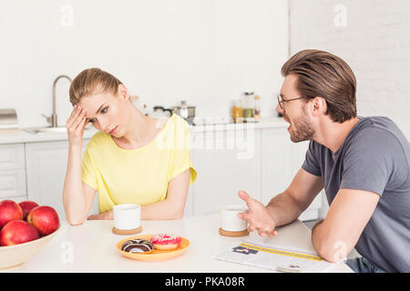 angry man screaming at upset girlfriend while she sitting at table with breakfast Stock Photo