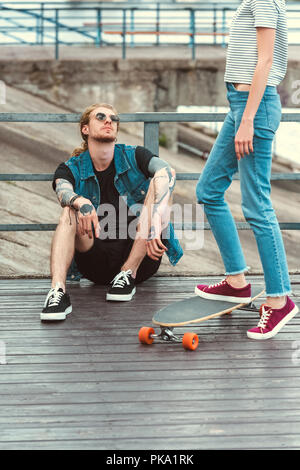 Handsome Stylish Tattooed Skater Sitting On Bridge Near Longboard Stock  Photo - Download Image Now - iStock