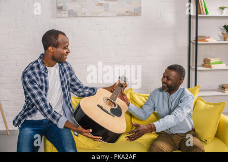 african american father and adult son holding acoustic guitar at home Stock Photo