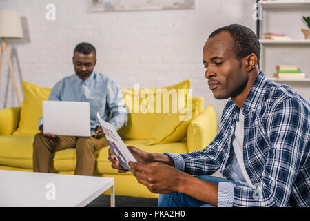young man reading newspaper and senior father using laptop behind Stock Photo