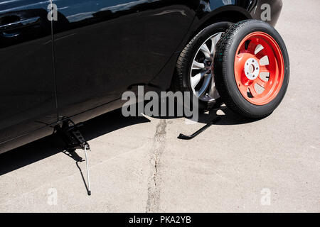 close up view of jack screw, wheel spanner and tire near broken car at street