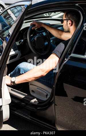 side view of stylish man in sunglasses closing door of his car at street Stock Photo