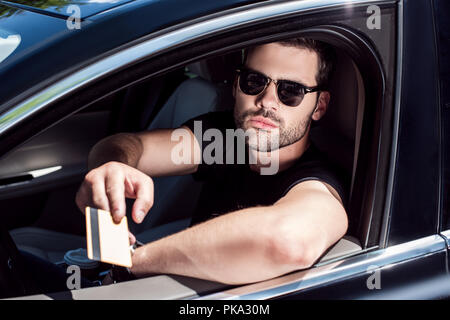 serious young man in sunglasses giving credit card while sitting in his car