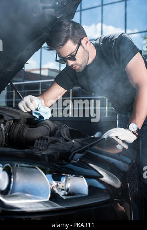 Handsome young man trying to repair a car engine, looking inside open ...