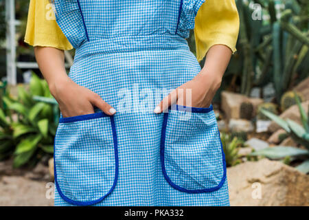 cropped shot of woman in apron standing with hands in pockets in greenhouse Stock Photo