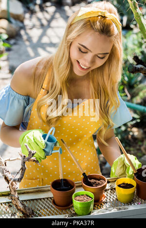 beautiful smiling young woman watering pots with small watering can Stock Photo