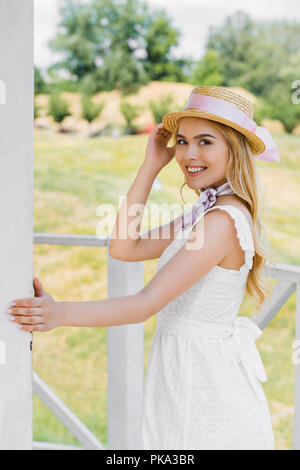 beautiful young woman in wicker hat and white dress smiling at camera Stock Photo