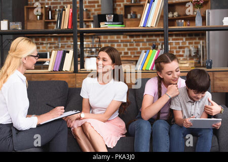 smiling female counselor talking to woman while her children using digital tablet on therapy session Stock Photo