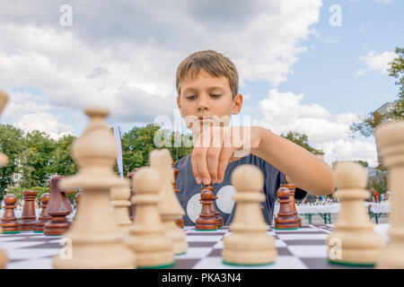 Kid playing chess at chessboard outdoors. Boy thinking hard on chess combinations Stock Photo