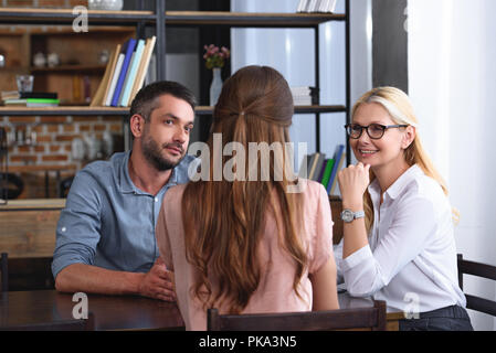 couple sitting at table during therapy session by female counselor in her office Stock Photo