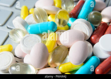 Pile of assorted medicine pills and capsules on gray keyboard, macro pharmaceutical background. Stock Photo