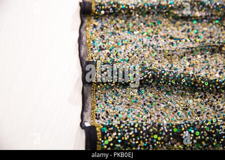 Black translucent fabric with green and yellow beads, lies on a white wooden table Stock Photo