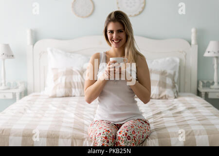 Young beautiful woman sitting on bed at home Stock Photo