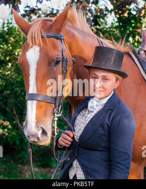 An elegent young woman stood with her horse dressed in traditional riding top hat and face veil Stock Photo