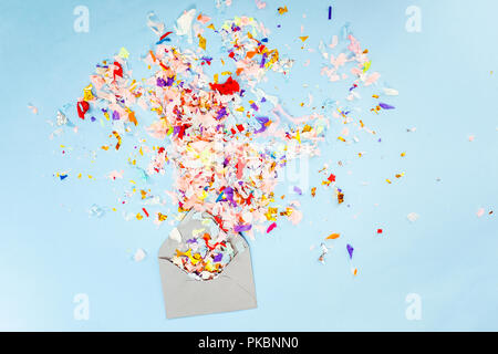 Envelope with party confetti explosion on pastel blue background. Stock Photo