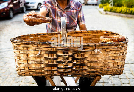 Street vendor selling simit (bread with sesame seeds) in basket and holding one of them to give the customer around Ankara Castle Stock Photo