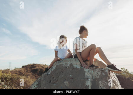 Two girls sit on a boulder looking out; Los Angeles, California, United States of America Stock Photo
