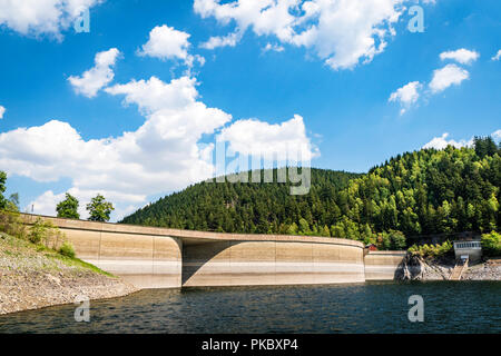 River with a dam surrounded by hills and pine trees under a blue sky Stock Photo