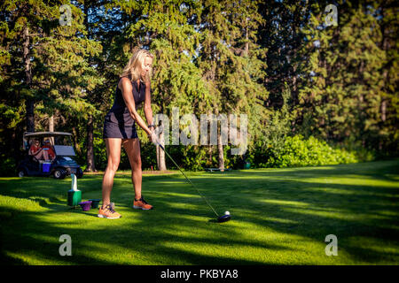 A digitally manipulated image of female golfer as she lines up her driver with the golf ball as two other golfers wait in the golf cart in the back... Stock Photo