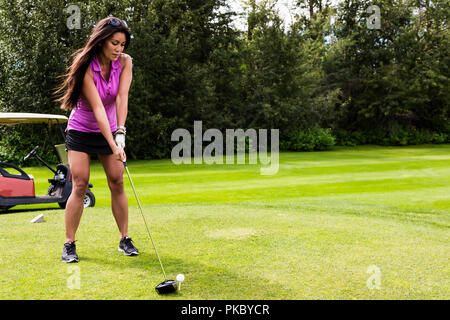 A female golfer lines up her driver to the golf ball as she sets up her shot on a tee; Edmonton, Alberta, Canada Stock Photo