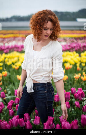 A woman with red hair stands in a field of tulips; Abbotsford, British Columbia, Canada Stock Photo