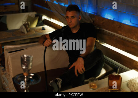 Handsome hipster man relaxing in the bar. Man smokes a hookah. Stock Photo