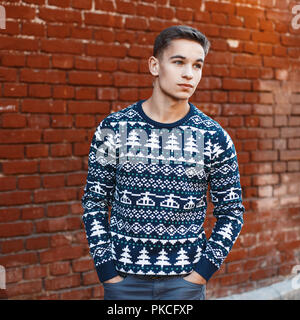 Young handsome man in a knit sweater with Christmas ornaments on a background of red brick wall Stock Photo